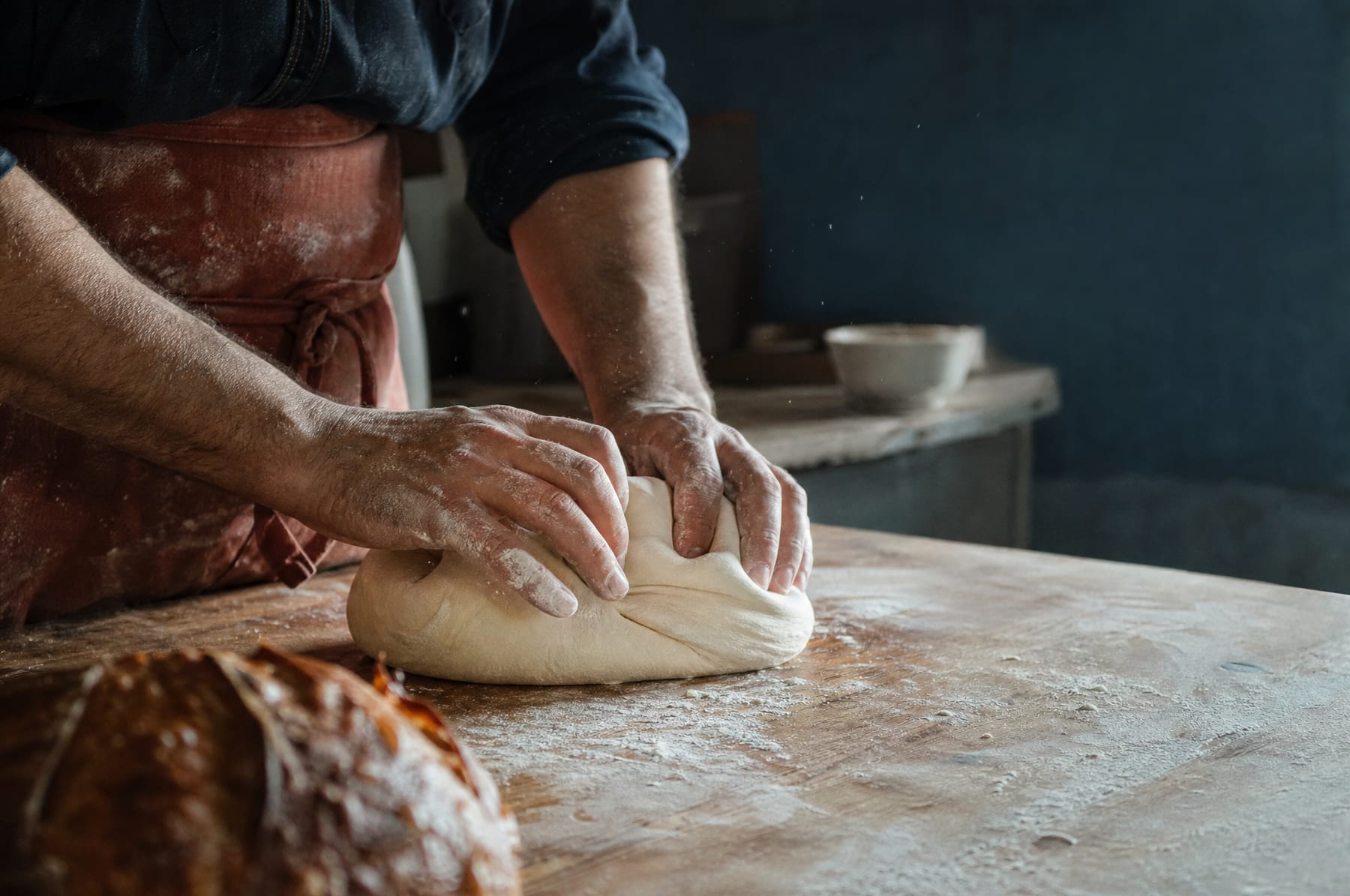 Des mains farinées plient une pâte sur un plan de travail en bois, dans un laboratoire de boulangerie.